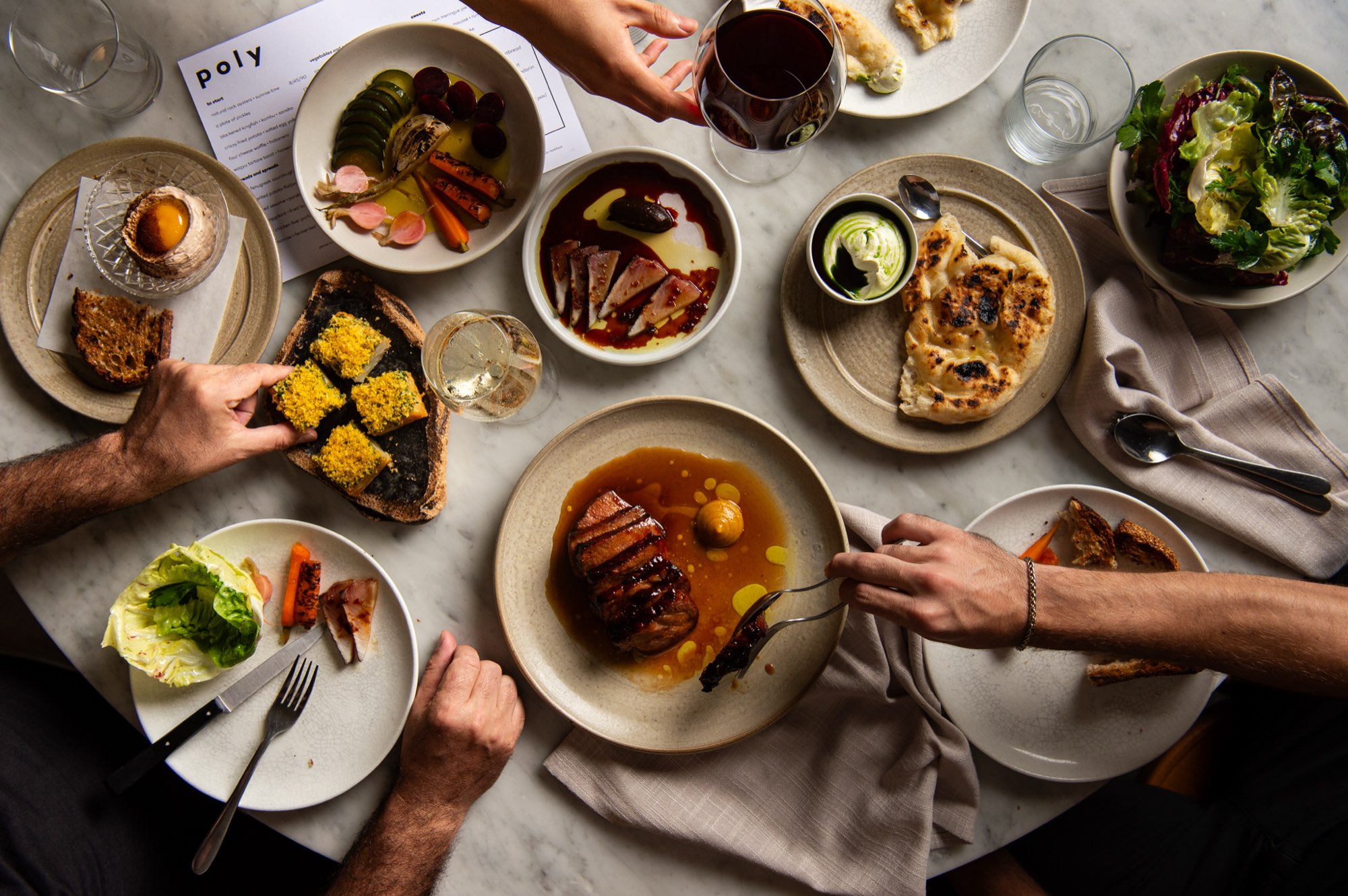 A shared table at Poly, Sydney, photographed from above with hands reaching in